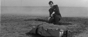 Movie still from “A Colt Is My Passport” (1967), directed by Takashi Nomura – A black and white photo of a man kneeling on the ground; Medium shot, High angle