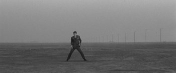 Movie still from “A Colt Is My Passport” (1967), directed by Takashi Nomura – A black and white photo of a man in a suit in a field; Wide shot, Low angle