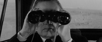 Movie still from “A Colt Is My Passport” (1967), directed by Takashi Nomura – A man in a suit looking through binoculars; Close Up shot, Over the shoulder angle