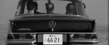 Movie still from “A Colt Is My Passport” (1967), directed by Takashi Nomura – Three men are sitting in the back seat of a car; Medium shot, Low angle