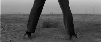 Movie still from “A Colt Is My Passport” (1967), directed by Takashi Nomura – A black and white photo of a man standing in front of a hole in the ground; Wide shot, Low angle