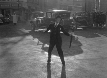 Movie still from “A Damsel in Distress” (1937), directed by George Stevens – A man in a suit and tie holding an umbrella in a parking lot; Wide shot, High angle