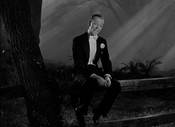 Movie still from “A Damsel in Distress” (1937), directed by George Stevens – A black and white photo of a man in a tuxedo sitting on a tree; Medium shot, Low angle