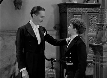 Movie still from “A Damsel in Distress” (1937), directed by George Stevens – A man and a woman in a suit and tie standing next to each other in front of an antique cabinet; Medium shot, High angle