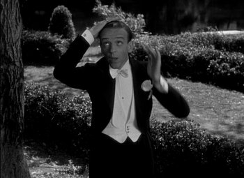 Movie still from “A Damsel in Distress” (1937), directed by George Stevens – A man in a suit and bow tie holding his hand up to his head; Medium shot, High angle