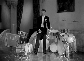 Movie still from “A Damsel in Distress” (1937), directed by George Stevens – A man in a tuxedo sitting in front of a bunch of drums; Wide shot, High angle