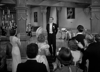Movie still from “A Damsel in Distress” (1937), directed by George Stevens – A black and white photo of a man standing in front of a group of people; Wide shot, High angle
