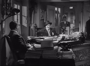 Movie still from “A Double Life” (1947), directed by George Cukor – A man sitting at a table in front of a pile of papers; Wide shot, High angle