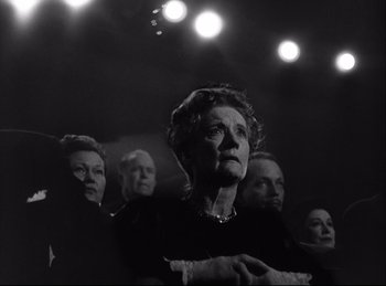 Movie still from “A Double Life” (1947), directed by George Cukor – An older woman standing in front of a group of people; Medium shot, Low angle