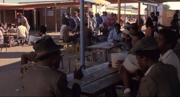 Movie still from “A Dry White Season” (1989), directed by Euzhan Palcy – A group of people sitting at a table outside; Wide shot, Over the shoulder angle