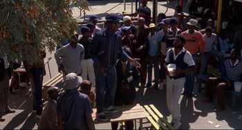 Movie still from “A Dry White Season” (1989), directed by Euzhan Palcy – A group of people standing around a table; Wide shot, Over the shoulder angle