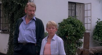Movie still from “A Dry White Season” (1989), directed by Euzhan Palcy – A man standing next to a young boy in front of a house; Medium shot, Low angle