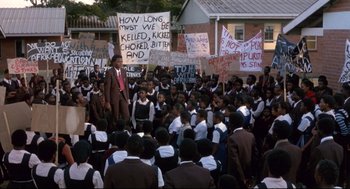 Movie still from “A Dry White Season” (1989), directed by Euzhan Palcy – A group of people protesting in front of a building; Wide shot, High angle