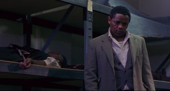 Movie still from “A Dry White Season” (1989), directed by Euzhan Palcy – A man standing next to another man on a bunk bed; Medium shot, Over the shoulder angle