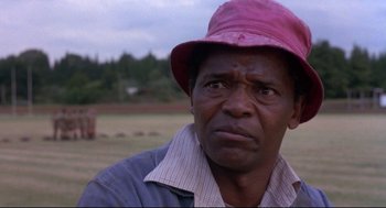 Movie still from “A Dry White Season” (1989), directed by Euzhan Palcy – An older man wearing a pink hat in a field; Close Up shot, Low angle