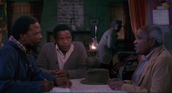 Movie still from “A Dry White Season” (1989), directed by Euzhan Palcy – A group of people sitting around a table; Medium shot, Over the shoulder angle