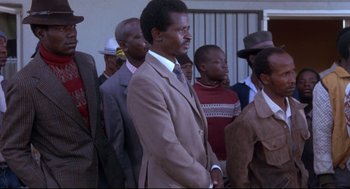 Movie still from “A Dry White Season” (1989), directed by Euzhan Palcy – A group of men standing next to each other in suits; Medium shot, Low angle