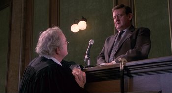 Movie still from “A Dry White Season” (1989), directed by Euzhan Palcy – A judge and a judge sitting in front of a microphone in a courtroom; Medium shot, Over the shoulder angle