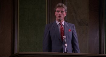 Movie still from “A Dry White Season” (1989), directed by Euzhan Palcy – A man in a suit and tie standing at a podium; Medium shot, Low angle