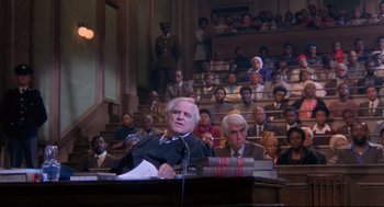Movie still from “A Dry White Season” (1989), directed by Euzhan Palcy – An older man is speaking at a podium in front of an audience; Wide shot, High angle