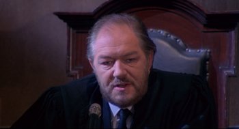 Movie still from “A Dry White Season” (1989), directed by Euzhan Palcy – A man with a beard and mustache is sitting in front of a microphone; Close Up shot, High angle