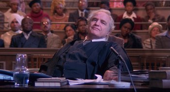Movie still from “A Dry White Season” (1989), directed by Euzhan Palcy – A judge sitting in front of a group of people; Medium shot, Low angle