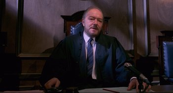 Movie still from “A Dry White Season” (1989), directed by Euzhan Palcy – A man sitting at a table in a courtroom; Medium shot, High angle