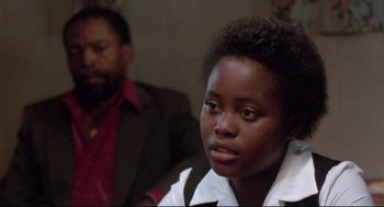 Movie still from “A Dry White Season” (1989), directed by Euzhan Palcy – A young woman sitting in front of a man in a suit; Close Up shot, Over the shoulder angle
