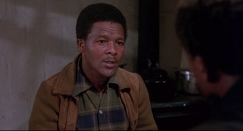 Movie still from “A Dry White Season” (1989), directed by Euzhan Palcy – A man sitting in front of a stove in front of a brick wall; Close Up shot, Over the shoulder angle