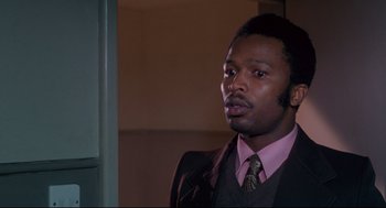 Movie still from “A Dry White Season” (1989), directed by Euzhan Palcy – A man wearing a suit and tie standing in front of a door; Close Up shot, Low angle