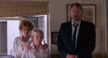 Movie still from “A Dry White Season” (1989), directed by Euzhan Palcy – A man and a woman standing next to a young boy; Medium shot, Low angle