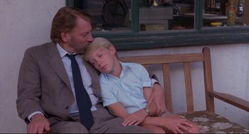 Movie still from “A Dry White Season” (1989), directed by Euzhan Palcy – A man and a boy sitting next to each other on a bench; Medium shot, Low angle
