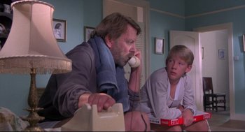 Movie still from “A Dry White Season” (1989), directed by Euzhan Palcy – A man sitting on a bed talking on the phone; Medium shot, Low angle