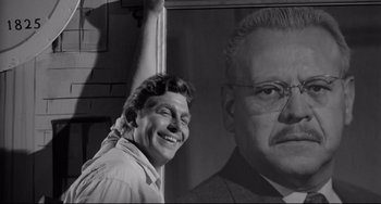 Movie still from “A Face in the Crowd” (1957), directed by Elia Kazan – A black and white photo of a man next to a picture of an older man; Medium shot, Low angle