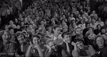 Movie still from “A Face in the Crowd” (1957), directed by Elia Kazan – An old photo of a group of people sitting in front of each other; Wide shot, High angle