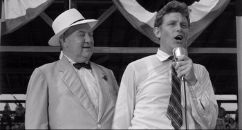 Movie still from “A Face in the Crowd” (1957), directed by Elia Kazan – Two men in suits and hats sing into microphones in front of an american flag; Medium shot, Low angle