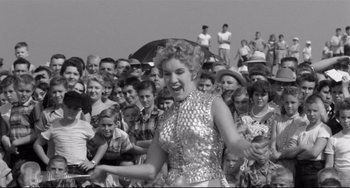Movie still from “A Face in the Crowd” (1957), directed by Elia Kazan – An old photo of a woman singing in front of a crowd; Medium shot, Low angle