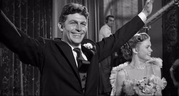 Movie still from “A Face in the Crowd” (1957), directed by Elia Kazan – A black and white photo of a man in a suit waving; Medium shot, Low angle