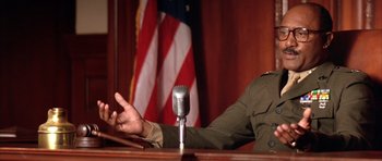 Movie still from “A Few Good Men” (1992), directed by Rob Reiner – A man sitting in front of a microphone in front of an american flag; Close Up shot, Low angle