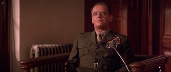 Movie still from “A Few Good Men” (1992), directed by Rob Reiner – A man in a military uniform sitting in front of a microphone; Medium shot, Low angle