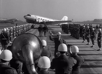 Movie still from “A Foreign Affair” (1948), directed by Billy Wilder – An old photo of a crowd of men standing on a runway with an airplane in the background; Wide shot, Low angle