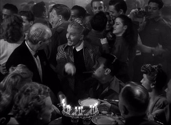 Movie still from “A Foreign Affair” (1948), directed by Billy Wilder – A group of people sitting around a table with lit candles on top of it; Medium shot, High angle