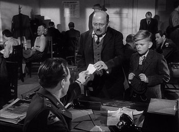 Movie still from “A Foreign Affair” (1948), directed by Billy Wilder – A man in a suit and tie handing a paper to another man in a suit and tie in front of another man; Medium shot, Over the shoulder angle