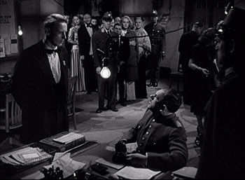 Movie still from “A Foreign Affair” (1948), directed by Billy Wilder – A man sitting in front of a group of people in a room; Wide shot, Over the shoulder angle