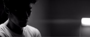 Movie still from “A Girl Walks Home Alone at Night” (2014), directed by Ana Lily Amirpour – A man in a white t - shirt is looking at the camera; Close Up shot, Low angle