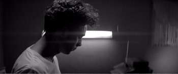 Movie still from “A Girl Walks Home Alone at Night” (2014), directed by Ana Lily Amirpour – A black - and - white photo of a man's face in the dark; Close Up shot, Low angle