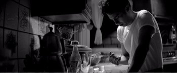 Movie still from “A Girl Walks Home Alone at Night” (2014), directed by Ana Lily Amirpour – A man in white shirt preparing food in a kitchen; Medium shot, Low angle