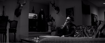 Movie still from “A Girl Walks Home Alone at Night” (2014), directed by Ana Lily Amirpour – A man sitting on a couch smoking a cigarette; Wide shot, Over the shoulder angle