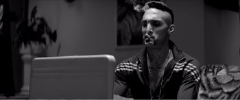 Movie still from “A Girl Walks Home Alone at Night” (2014), directed by Ana Lily Amirpour – A man smoking a cigarette while sitting in front of a computer; Close Up shot, Low angle