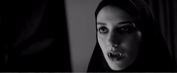 Movie still from “A Girl Walks Home Alone at Night” (2014), directed by Ana Lily Amirpour – A woman with a black head scarf on; Close Up shot, Low angle